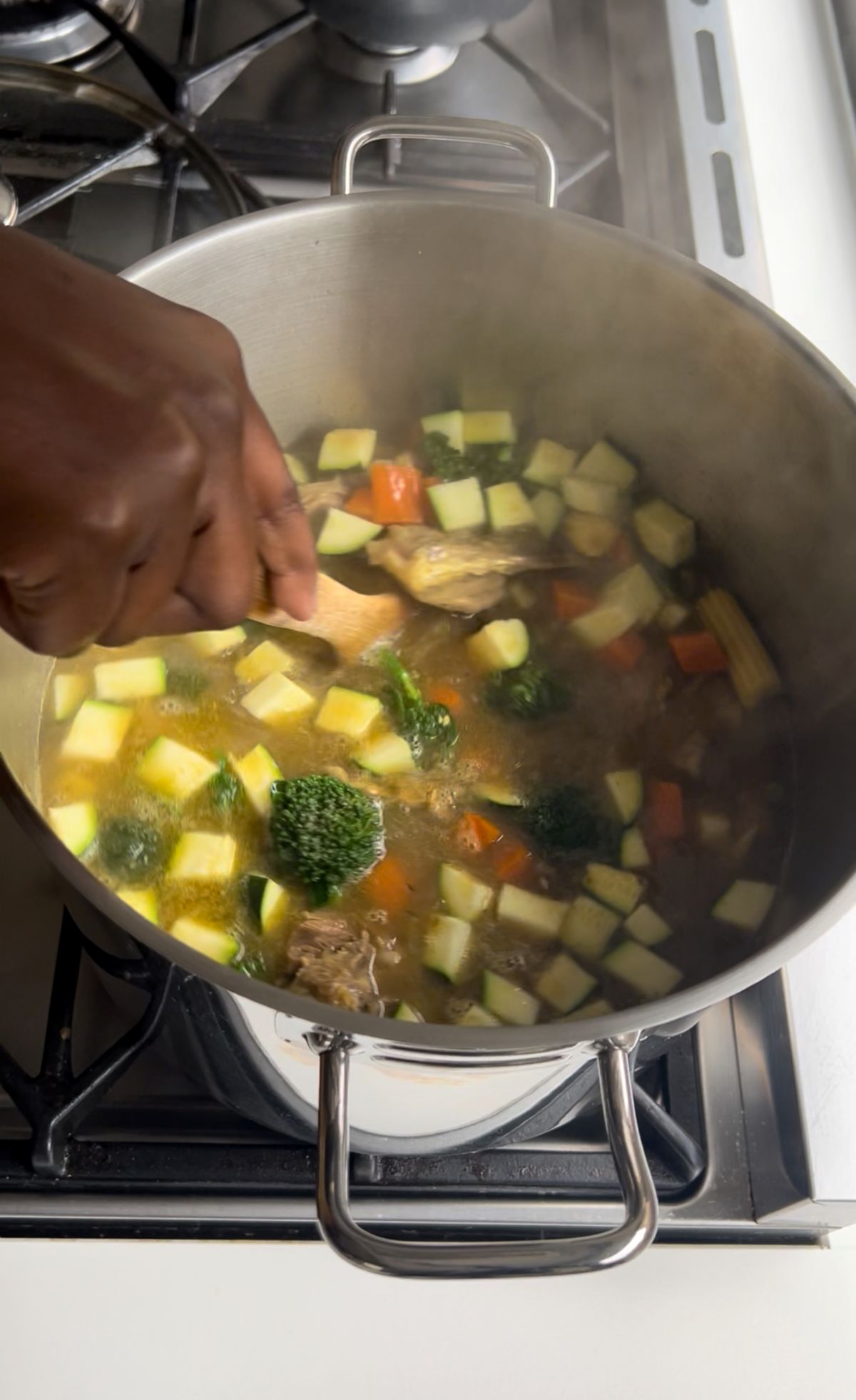 A mix of vegetables including mushrooms, broccoli, mini corn, and bean sprouts being added to the pot in large pieces.