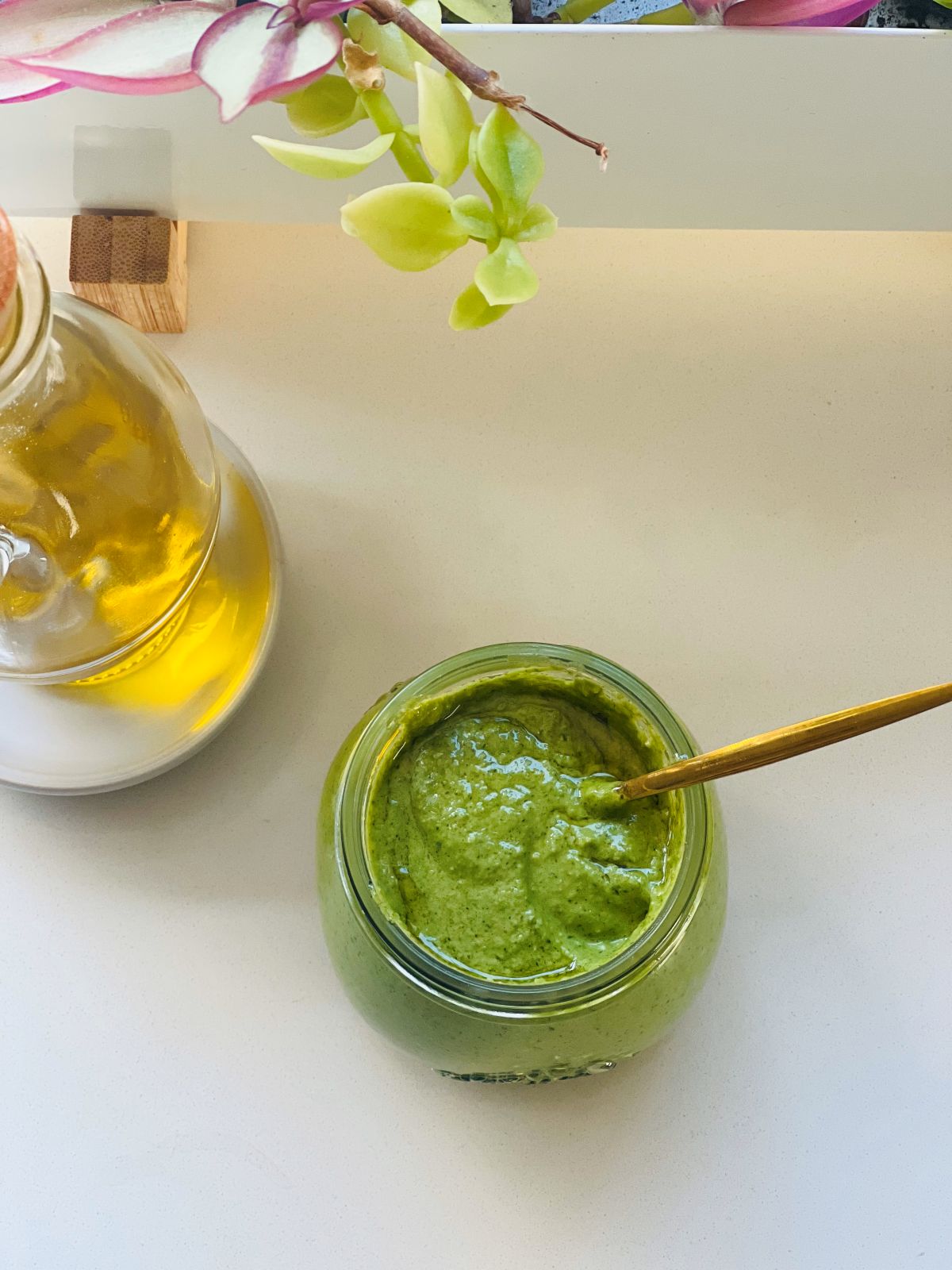 Close-up of blended coriander pesto recipe in a glass jar with a thin layer of olive oil on top.