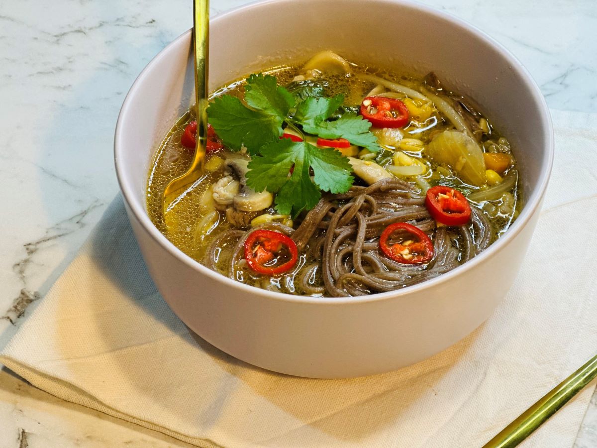 Finished pork noodle soup in a bowl topped with spring onions, chili oil, and red-pepper flakes.