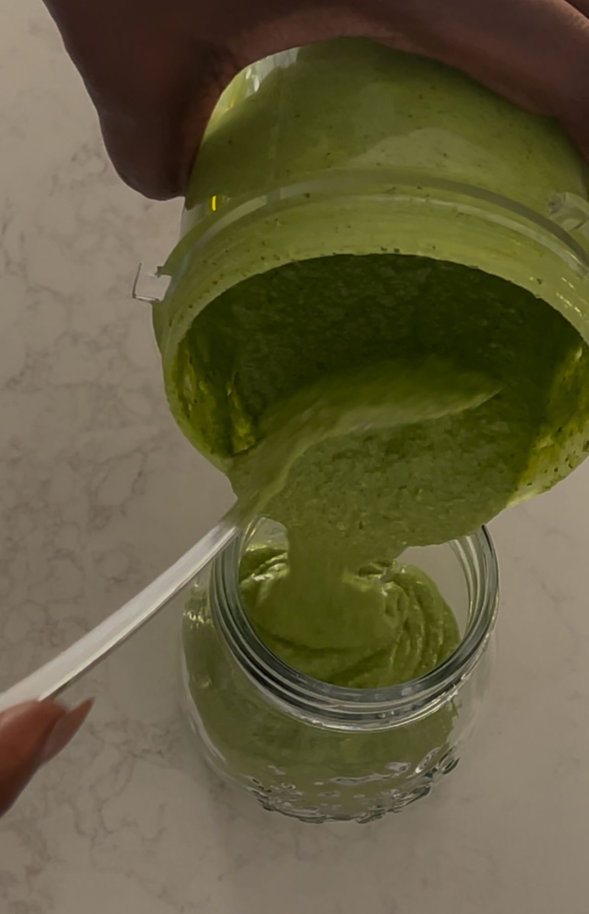 Coriander pesto recipe being poured into a glass jar for storage with a swirl of olive oil on top.