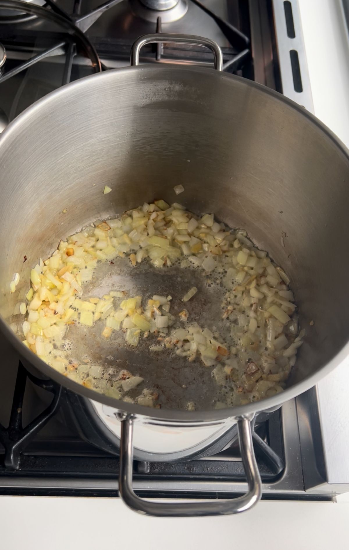 Garlic, fresh ginger, and sliced onions sizzling in olive oil in a deep pan over medium heat.