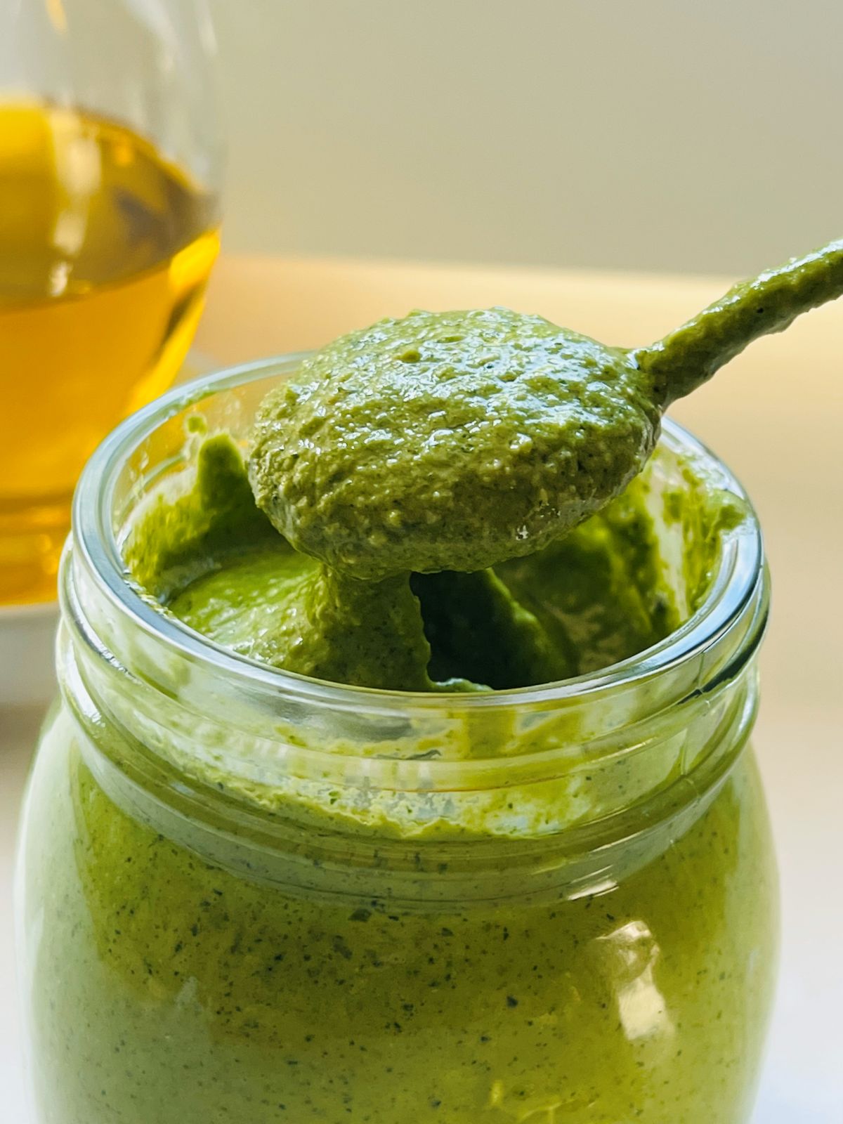 Spoonful of vibrant coriander pesto recipe lifted from the jar, showing its rich green texture.